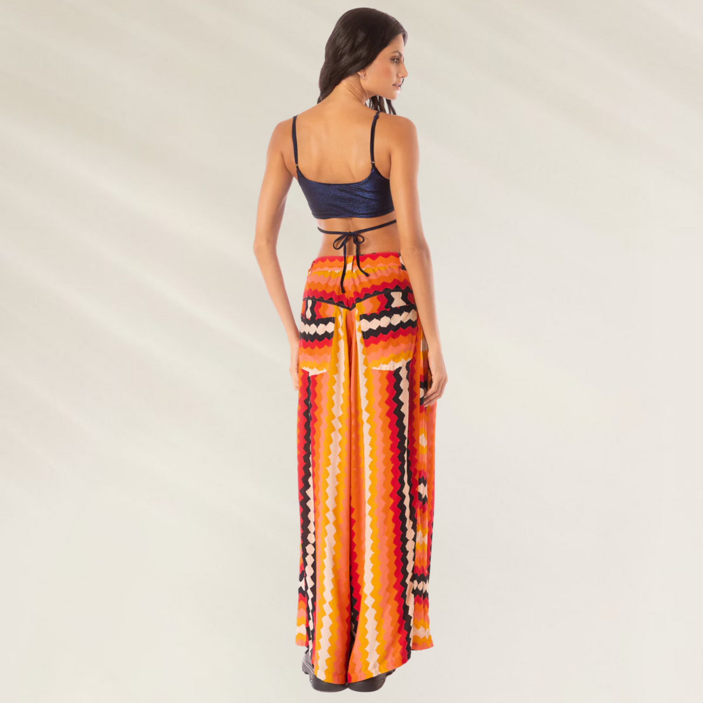 Modelo de costas usando Calças Maaji Sabine Hyperflares estampadas em laranja vermelho e amarelo com cós alto e perna ampla