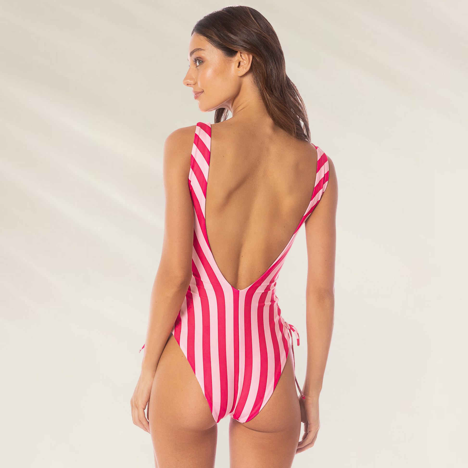 Mulher vestindo Fato de Banho Maaji Grape One Piece – Apple Stripes com listras rosa e branca e costas abertas
