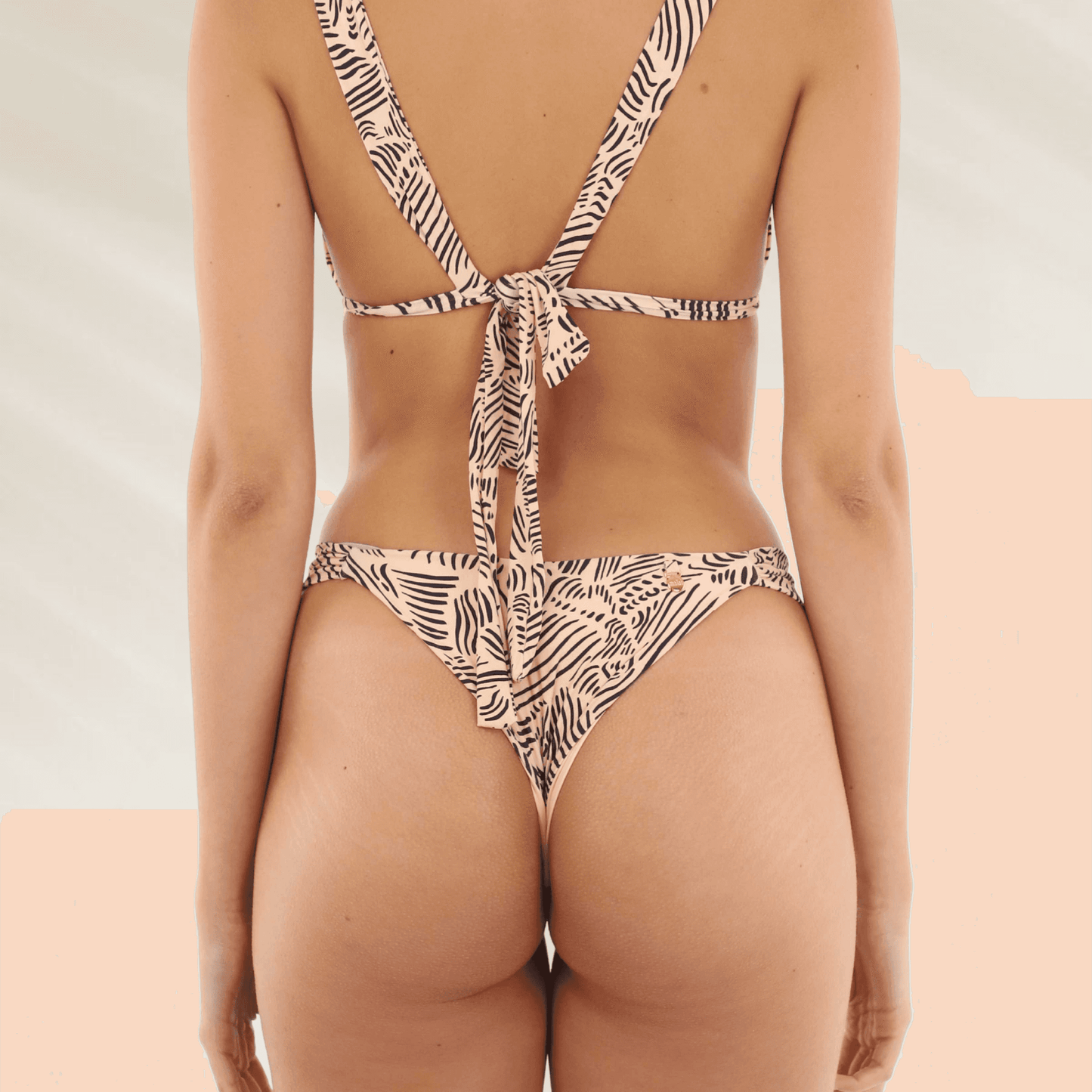 Vista traseira de modelo usando Cueca Malai Reversível com Corte Latino Cavado. Estampa zebrada bege e preta e top amarrado