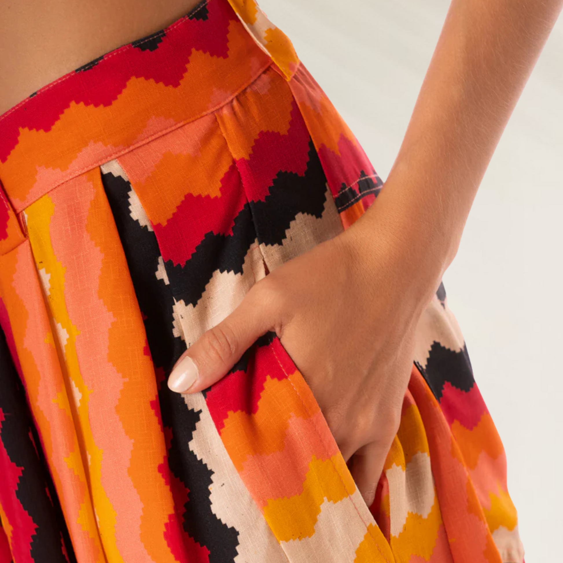 Calças Maaji Sabine Hyperflares estampadas em tons de laranja vermelho e preto detalhe de bolso com mão feminina
