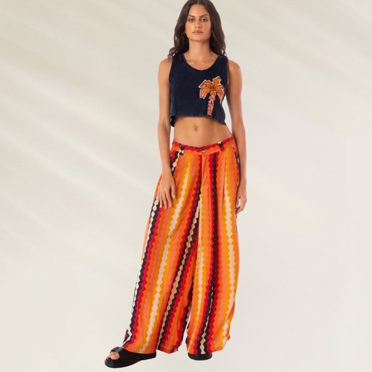Modelo usando Calças Maaji Sabine Hyperflares listradas largas em tons de laranja vermelho e preto com top cropped azul e chinelos
