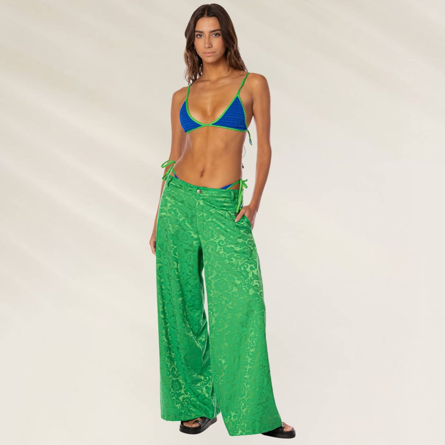 Mulher usando calças largas texturizadas verdes da marca Maaji com um biquíni azul