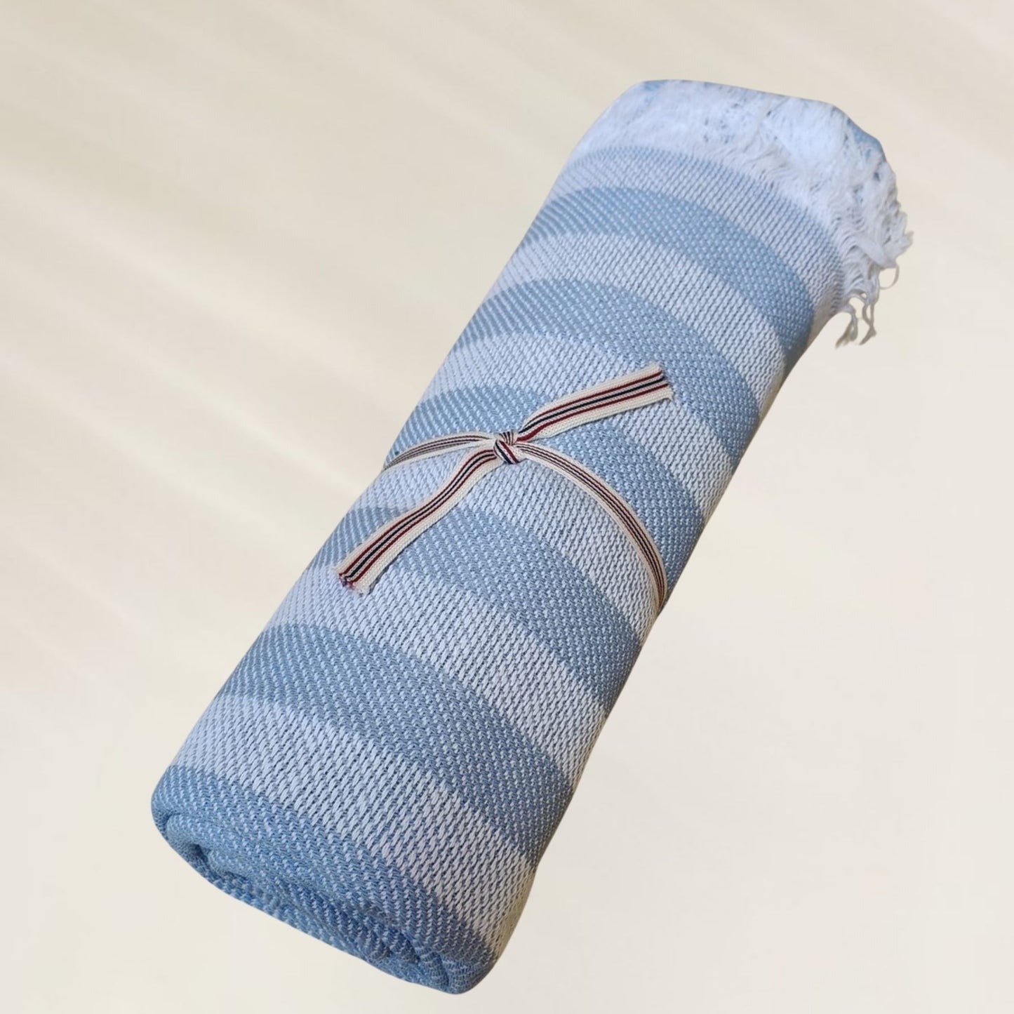 Toalha Ocean Breeze da Kalua em tons de azul, dobrada e presa com fita, ideal para praia