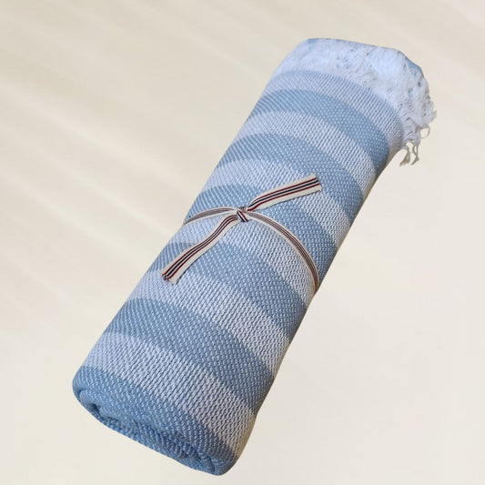Toalha Ocean Breeze da Kalua em tons de azul, dobrada e presa com fita, ideal para praia