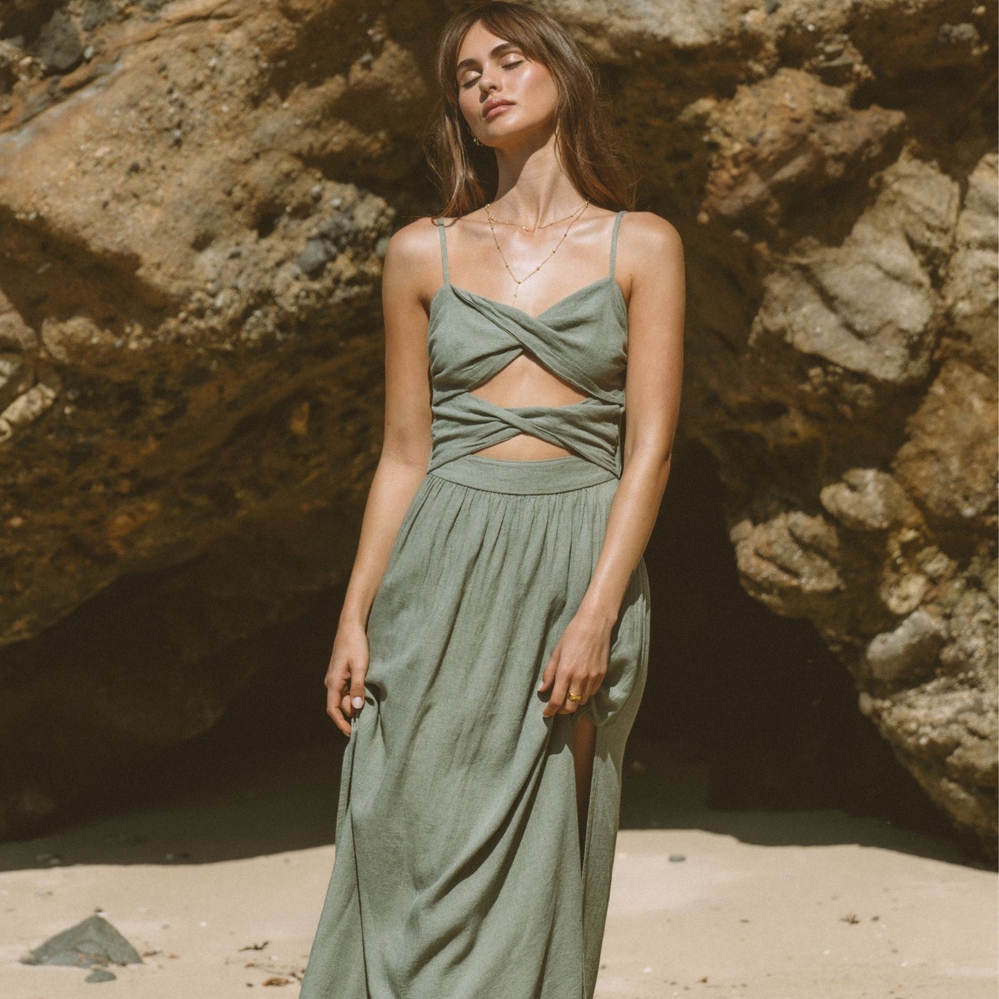 Modelo usando Vestido Maxi Verde Cut-Out em praia com fundo rochoso e iluminado pelo sol